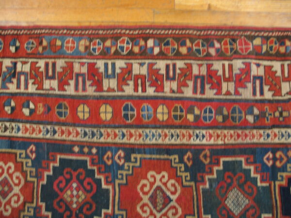 Red and blue geometric rug featuring intricate borders and low pile texture on wooden planks.