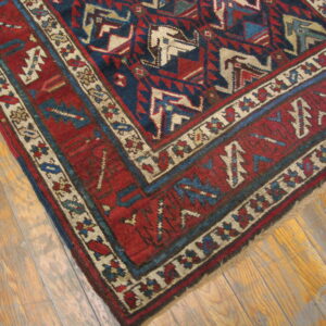 Red and navy geometric rug with beige borders rests on distressed natural wood plank flooring.