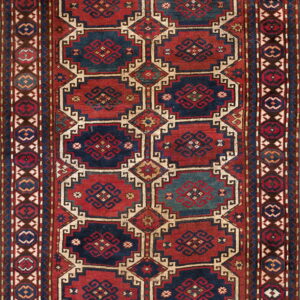 Geometric rug with stepped panels in deep red and navy blue, bordered by small octagonal motifs.