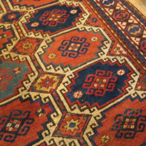 Red and navy geometric rug with cream outlining and complex medallions visible on wood flooring.