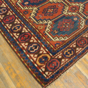 Geometric rug featuring bold red, navy, and cream patterns resting on light-colored wooden planks.