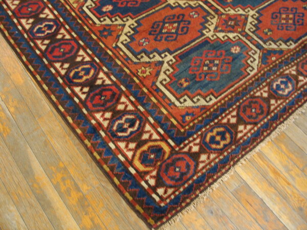 Geometric rug featuring bold red, navy, and cream patterns resting on light-colored wooden planks.