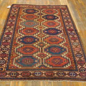 Traditional geometric rug in rust red and indigo blue with multiple borders on hardwood floor.