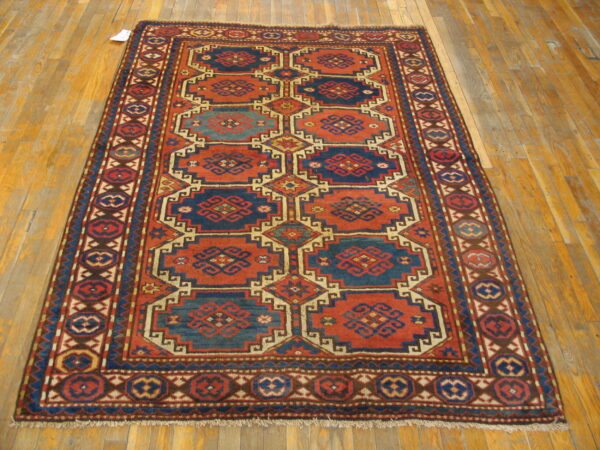 Traditional geometric rug in rust red and indigo blue with multiple borders on hardwood floor.