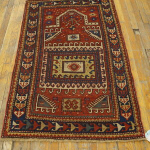 A red and navy geometric accent rug with a low pile is displayed on worn hardwood floorboards.