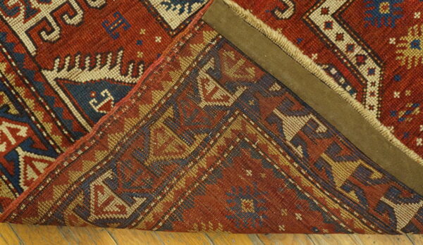 Red and blue geometric rug is folded over, displaying the knotted reverse side on wood flooring.