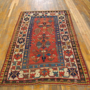 A low-pile rug in rust red, blue, cream, and brown featuring tribal geometric patterns on a wood plank floor.