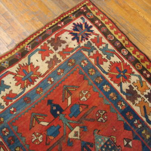 Geometric red, blue, and ivory patterned rug corner detail lying on distressed hardwood flooring.