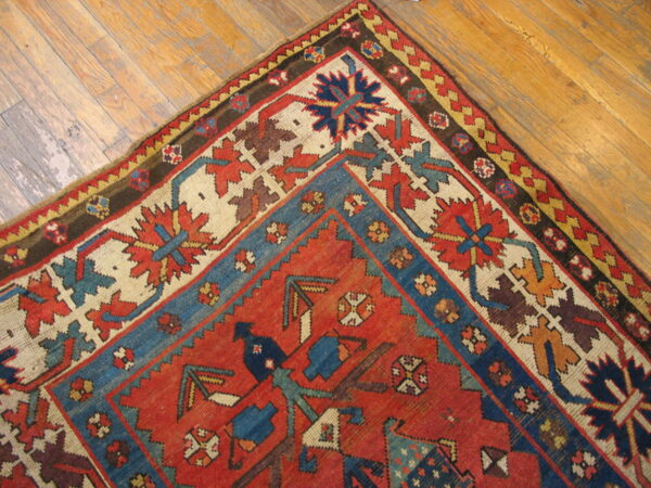 Geometric red, blue, and ivory patterned rug corner detail lying on distressed hardwood flooring.