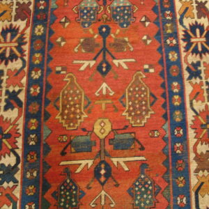 Red-orange field rug with complex geometric patterns, stylized bird motifs, and navy and ivory borders.