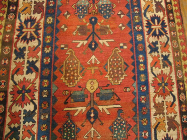 Red-orange field rug with complex geometric patterns, stylized bird motifs, and navy and ivory borders.