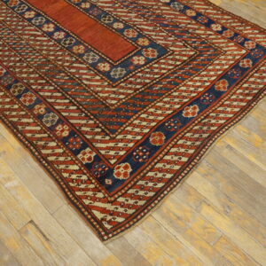 Rust red and navy blue geometric flatweave rug with cream patterns rests on weathered wood planks.