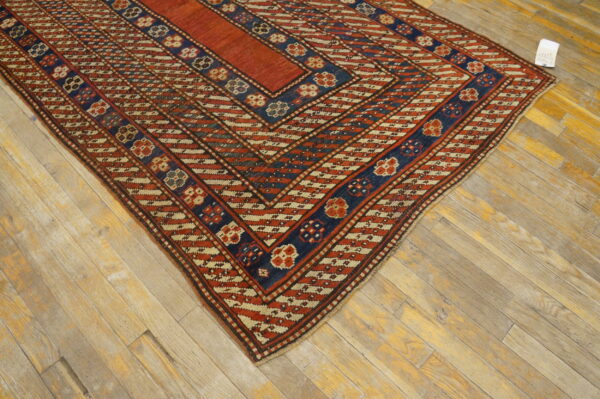 Rust red and navy blue geometric flatweave rug with cream patterns rests on weathered wood planks.