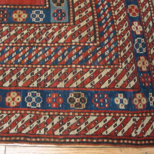 Red and blue geometric rug border with diagonal stripes and stylized medallions on a natural wood floor.