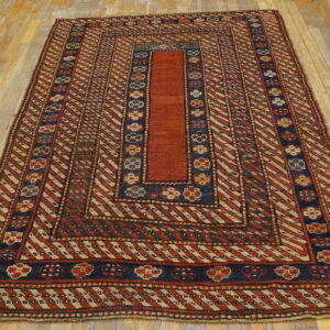 Red, navy, and tan geometric rug featuring diagonal stripes and floral borders on light wood flooring.