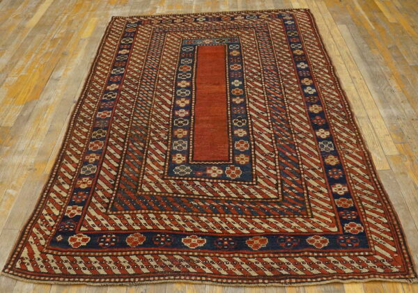 Red, navy, and tan geometric rug featuring diagonal stripes and floral borders on light wood flooring.