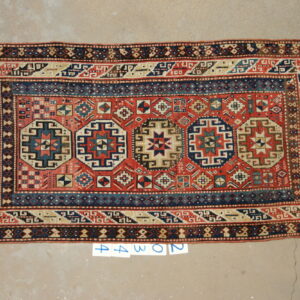 Low pile rug featuring a red field, navy geometric medallions, and tan borders on concrete flooring.