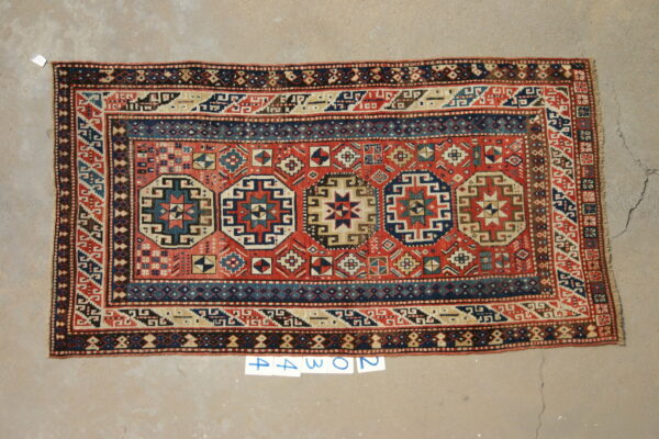 Low pile rug featuring a red field, navy geometric medallions, and tan borders on concrete flooring.