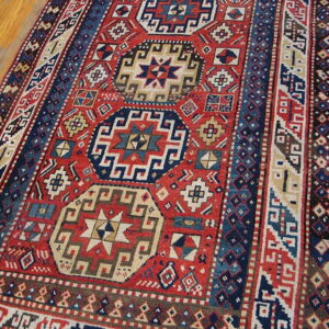 Red runner rug with navy blue geometric medallions and elaborate striped borders on wood flooring.