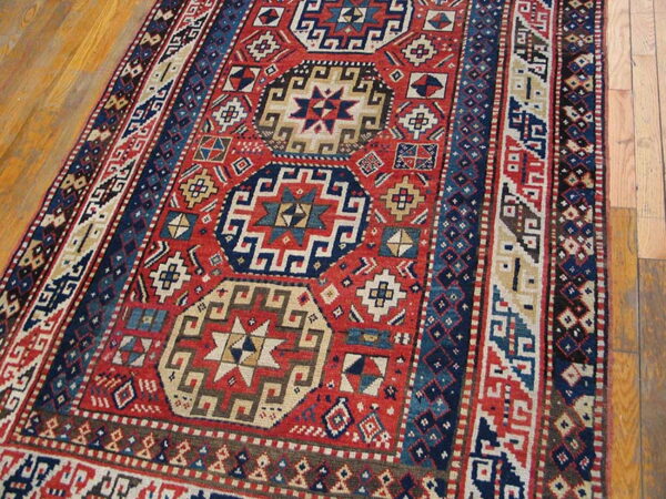 Red runner rug with navy blue geometric medallions and elaborate striped borders on wood flooring.