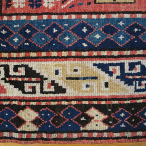 Textured rug detail with geometric patterns in navy, red, and cream, resting on wood flooring.