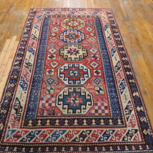 Red and blue geometric patterned rug with low pile displayed on light brown wood flooring.