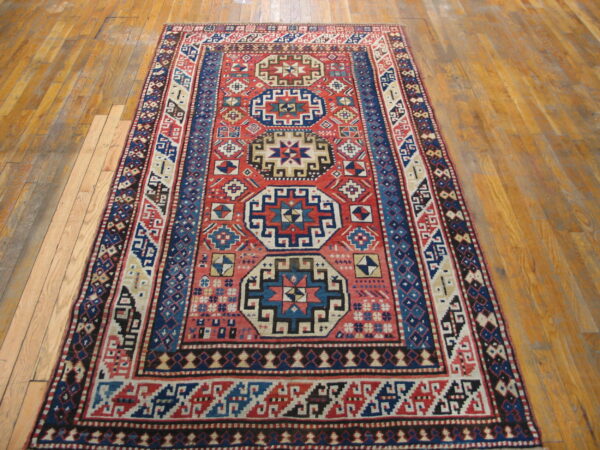 Red and blue geometric patterned rug with low pile displayed on light brown wood flooring.