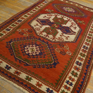 Geometric flatweave rug in rust red, navy, green, and cream patterns on distressed wide wooden floorboards.