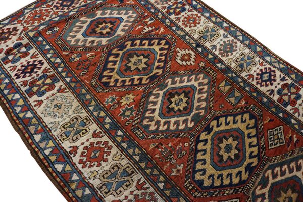 Geometric rug featuring large blue and gold medallions on a red field with patterned cream borders.