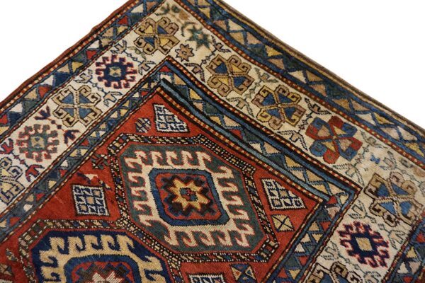 Corner detail of a patterned rug in red, blue, and cream with complex geometric borders.