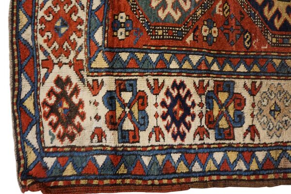 Low pile rug corner displays dense geometric borders and medallions in rust, cream, navy, and teal.