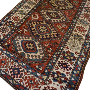 Geometric rug with a central red field, navy blue stepped medallions, and detailed cream and blue borders.