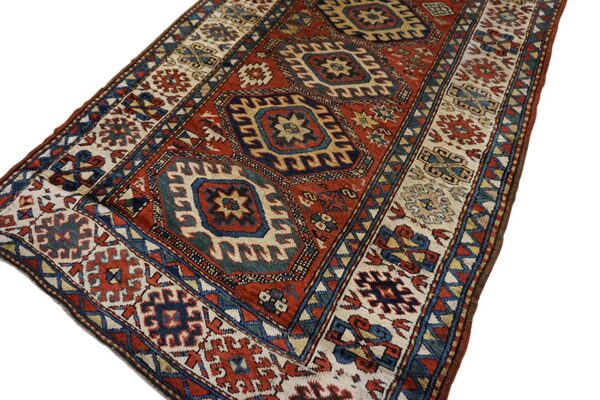 Geometric rug with a central red field, navy blue stepped medallions, and detailed cream and blue borders.