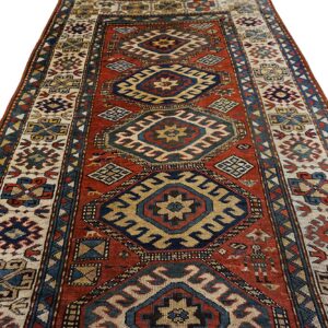 A rust red runner rug featuring geometric medallions in navy blue, beige, and yellow.