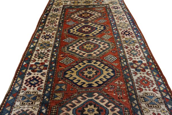 A rust red runner rug featuring geometric medallions in navy blue, beige, and yellow.