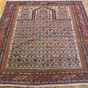 Traditional rug featuring stylized geometric patterns in red, cream, and blue on a glossy wooden floor.