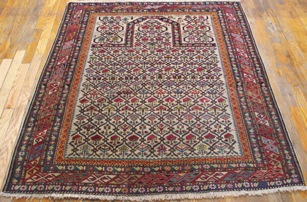 Traditional rug featuring stylized geometric patterns in red, cream, and blue on a glossy wooden floor.