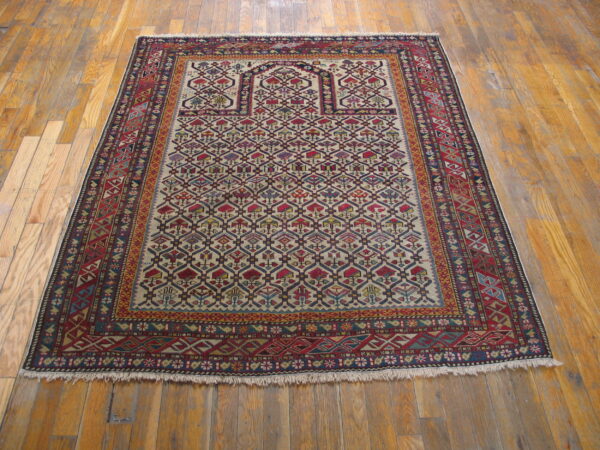 Red and blue geometric rug featuring a detailed lattice pattern over a cream field on warm wood flooring.