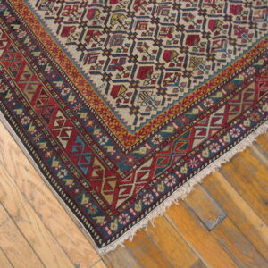 Tight weave rug with complex red, blue, and beige geometric patterns rests on light brown wood flooring.