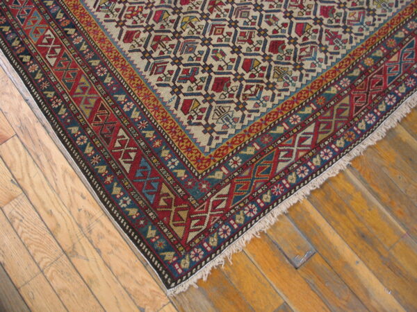 Tight weave rug with complex red, blue, and beige geometric patterns rests on light brown wood flooring.