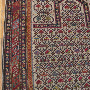 Detailed view of a cream rug with red and blue geometric patterns and borders beside light hardwood flooring.