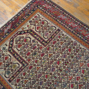 Low-pile rug corner with red, blue, and cream geometric designs placed on light wooden plank flooring.