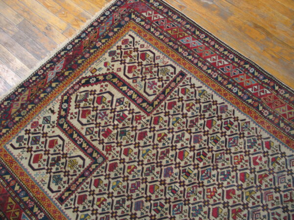 Low-pile rug corner with red, blue, and cream geometric designs placed on light wooden plank flooring.