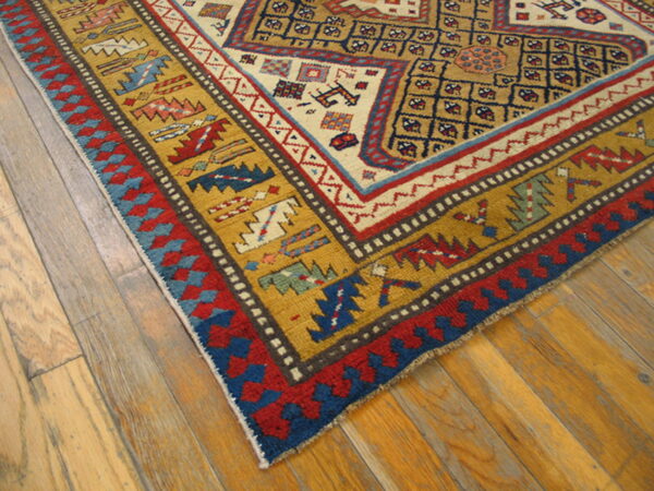 Geometric rug border in mustard yellow, red, blue, and cream lying on light natural hardwood planks.