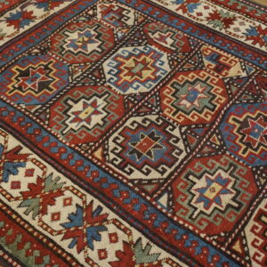 Low-pile rug with red, blue, and cream geometric tribal patterns resting on light hardwood flooring.