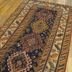 Geometric rug with blue, rust, cream, and yellow patterns, featuring multiple borders on aged wood flooring.