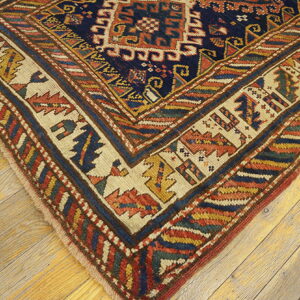 Detailed corner of a traditional rug with navy, red, yellow, and cream patterns resting on distressed wood floors.
