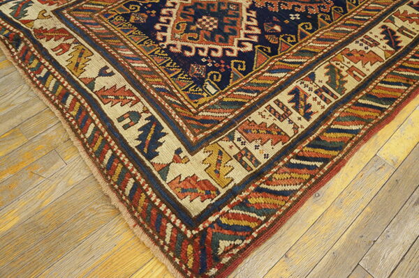 Detailed corner of a traditional rug with navy, red, yellow, and cream patterns resting on distressed wood floors.
