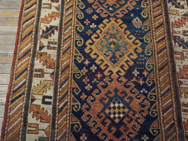 Geometric rug runner with navy, ochre, rust, and cream colors lying on distressed wood flooring.