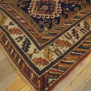 Navy blue geometric rug with wide cream and multi-colored borders on distressed wood planks.